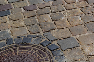 Old metal sewer hatch in the middle of the road, laid out of a smooth paving stone