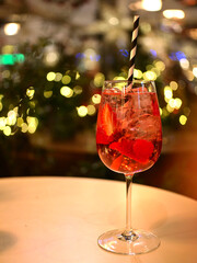 Gin Strawberry cocktail, in a large glass with ice cubes and straw. Bokeh in background.
