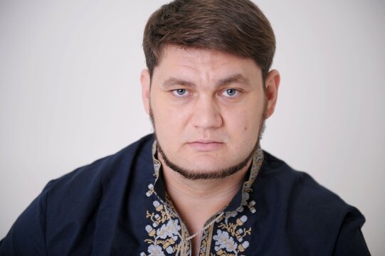 strong confident look of blue eyes of man in blue shirt with embroidery in front frowning forehead moving eyebrows who opened cancer eyes thin beard narrow lips concept power of confidence