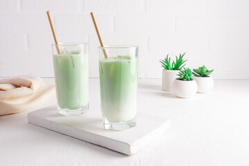 Obraz na płótnie Canvas Matcha latte tea in tall glasses with straw on a white wooden board. a healthy drink. purification of the body, improvement of metabolism.