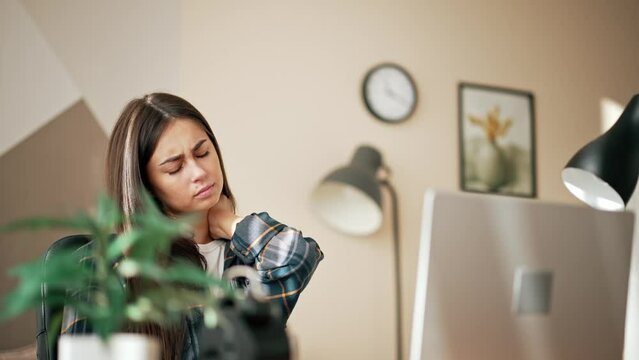 Tired overworked female, sedentary lifestyle concept. Young woman kneading her neck with her hands after long working day in home office. Closed eyes and relaxes, makes herself back and neck massage.