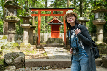 portrait of cheerful Asian Korean girl traveler looking into distance while visiting a historic park with red torii gate and ancient toro lamps at Kasuga Grand Shrine in nara japan.