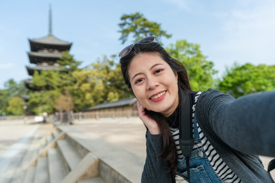 self portrait of smiling asian Japanese female visitor looking at camera with gojunoto pagoda of kofuku-ji temple at background in nara japan on a sunny day in spring