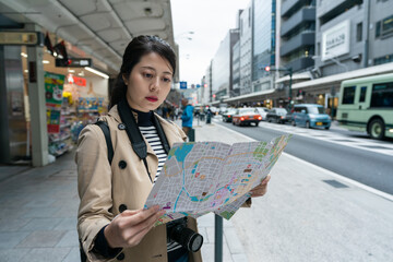 portrait of asian chinese girl tourist reading route map with concentration at a roadside bus...