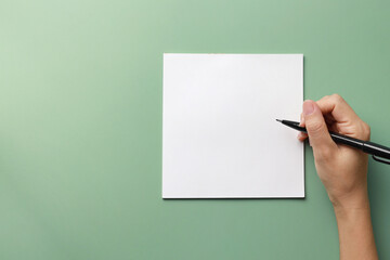 Hand with pen and paper on green background