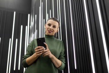 Obraz premium woman with mobile phone near black wall with vertical led lamps
