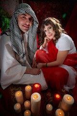 Portrait of young arabian muslim couple in traditional clothes in cozy room with candles. Fabulous photo shoot in easten style with male and female model like in a harem with a sultan and an odalisque