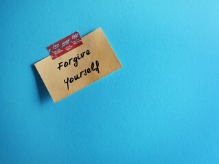 Stick note on blue copy space background with handwritten text FORGIVE YOURSELF, concept of learning to fully accept whatever you did - let go any resentment you have made significant mistakes