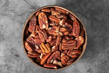 Pecan on dark background. Pecans in a coconut bowl. healthy fat. Heap shelled Pecans nut. Close up. Keto diet. Studio shoot. Top view