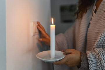 Energy crisis. Hand in complete darkness holding a candle trying to turn on light during a power...