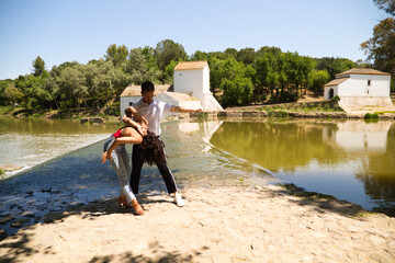 beautiful woman and handsome man latinos dancing bachata are dancing by the river in the forest. The couple do different postures while dancing. Dancing concept and expressions.