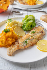 Pan fried  fish fillet with mashed potato, pumpkin puree and broccoli on a plate on white background