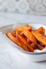 Sweet potato French fries chips in a white enamel dish bowl. On a marble background