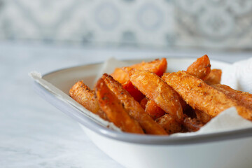 Sweet potato French fries chips in a white enamel dish bowl. On a marble background