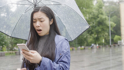 Young asian woman receiving break up message, standing in rain under umbrella