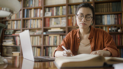 Beautiful Vietnamese woman student spending time in university library with laptop and notebooks