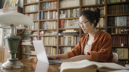 Young woman asian student sitting in library with laptop, studying or working
