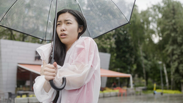 Young asian woman with umbrella feeling cold in the rain, waiting for taxi