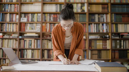 Female architect working on a blueprint in a university library, diligent student