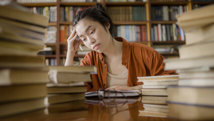 Upset asian female student sitting behind stacks of books, academic pressure