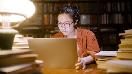Concentrated asian student in eyeglasses working late on laptop at city library