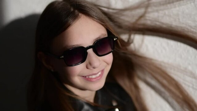 Slow motion video of a stylish child in leather jacke with glasses , the wind blows in her face and inflates the hair