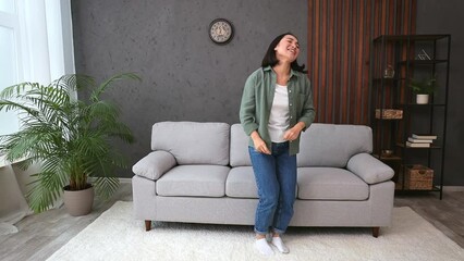 Full body young woman of Asian ethnicity wears casual clothes fancy dance waving rising have fun enjoy relax near sofa stay at home hotel flat rest relax spend free spare time in living room indoor