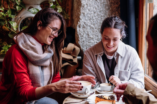 Two Happy Female Friends Talk And Catch Up In A Modern Coffee During Winter