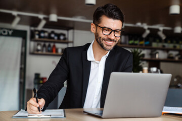 Young businessman using laptop and writing notes at office