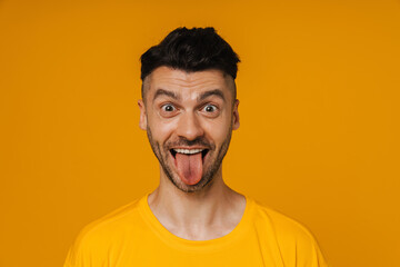 Obraz premium Joyful man showing tongue at camera isolated over yellow background