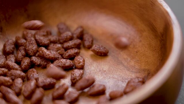 Chocolate cereal puffed rice flakes. Falling crispy popped breakfast grains into a wooden bowl. Macro. Rotation