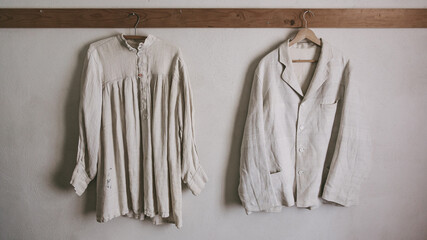 Vintage men's shirt and women's dress hang on a hanger against a white wall.