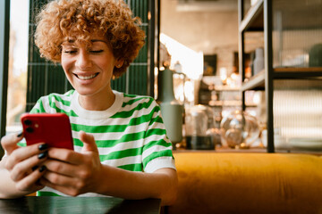 Mid white woman with curly hair smiling and using cellphone in cafe