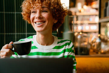 Fototapeta premium Mid white woman with curly hair smiling and drinking coffee in cafe