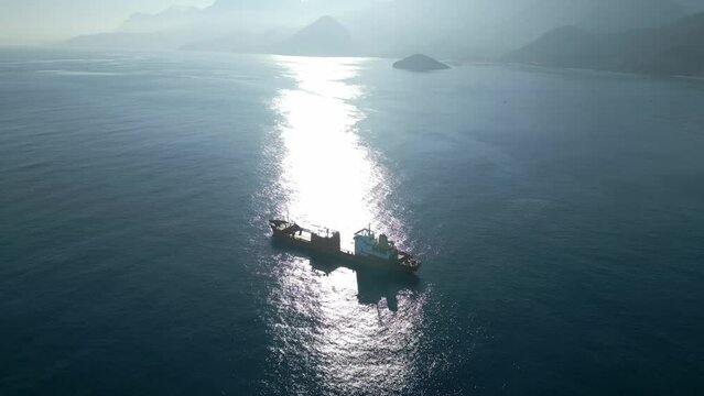 The camera flies around a chemical tanker drifting at sunset near the coastline with mountains. High quality 4k footage