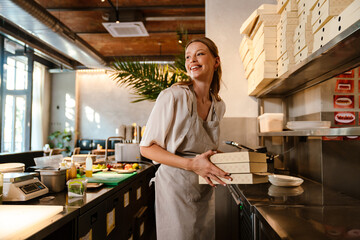 Young woman holding food boxes while working in restaurant kitchen - obrazy, fototapety, plakaty