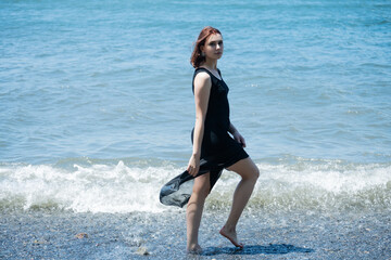 Young woman in black dress walking along the beach.