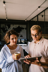 Two multinational colleagues using tablet while standing in office