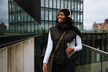 Smiling african woman holding digital tablet while walking outdoors