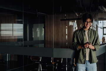Positive asian business man using smartphone while standing in modern office space