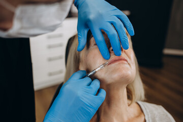 Botox, injection and antiaging with a senior woman in studio on a gray background with hands in gloves for treatment. Wrinkles, wellness and cosmetics with a mature female patient and plastic surgeon