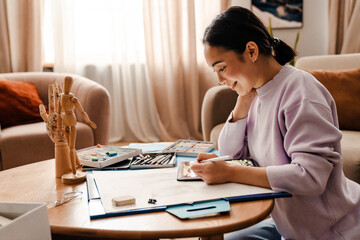 Smiling asian woman drawing on digital tablet with stylus at home