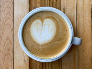 A cup of coffee latte on a wooden table. A mug of flat white coffee on a wooden background. Coffee art. Heart flower shape latte art. Copy space