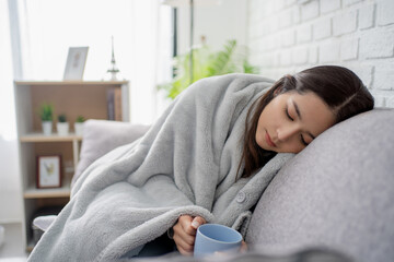 Feeling sick. Sick young women covered with blanket resting at home while sitting on the sofa