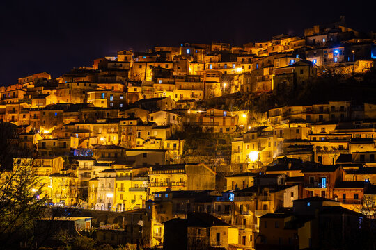 A stunning night photo of the cityscape of Tiriolo, a town in the province of Catanzaro, Calabria, Italy. The lights of the houses and streets contrast with the dark silhouette of the mountains