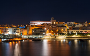 Fototapeta na wymiar A night view of Otranto, a picturesque town on the Adriatic coast of Puglia, Italy. The lights of the buildings and the harbor are reflected in the calm water.