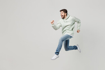Fototapeta na wymiar Full body side view overjoyed cheerful happy excited young caucasian man wear mint hoody jump high run fast hurry up isolated on plain solid white background studio portrait. People lifestyle concept.