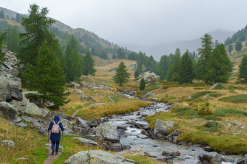 Fototapeta na wymiar A hiker enjoys the scenic beauty of De Vallée de la Clarée in Hautes-Alpes, France, on a rainy day. The valley is known for its alpine landscapes, waterfalls and mountain lakes.