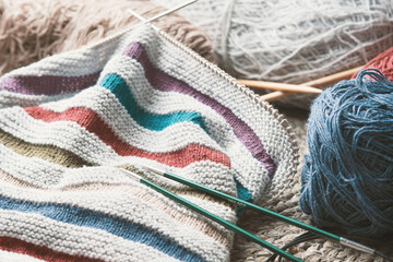 Knitted work in progress. Unfinished striped hat, skeins of cotton yarn and knitting needles.
