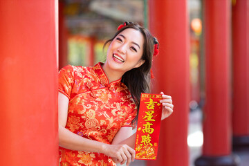 Asian woman in red cheongsam qipao dress is holding blessing fortune card saying to be blessed by a lucky star inside Chinese Buddhist temple during lunar new year for best wish and good luck concept